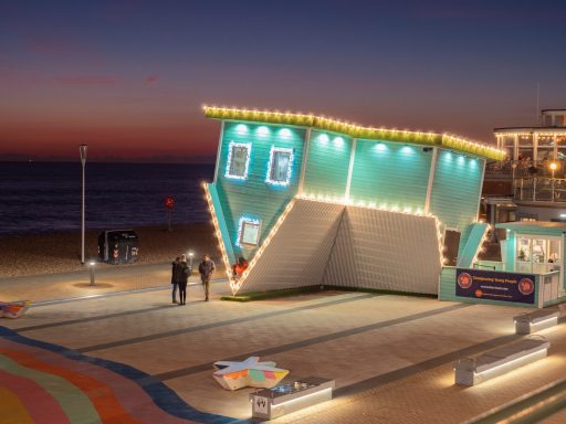 Colorful building with lights at sunset, located near the beach. Couples walking nearby.